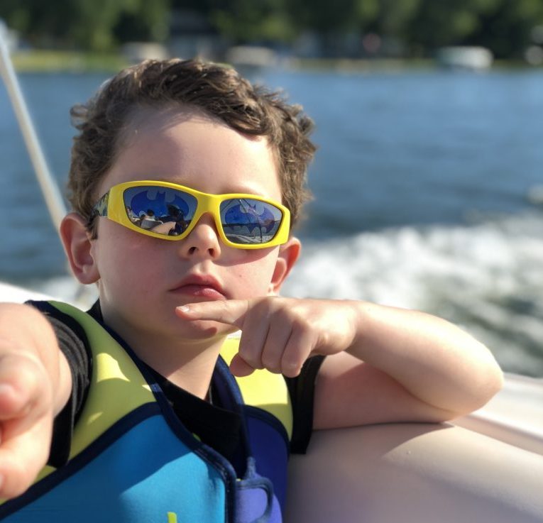 School age boy boat wake life vest sunglasses