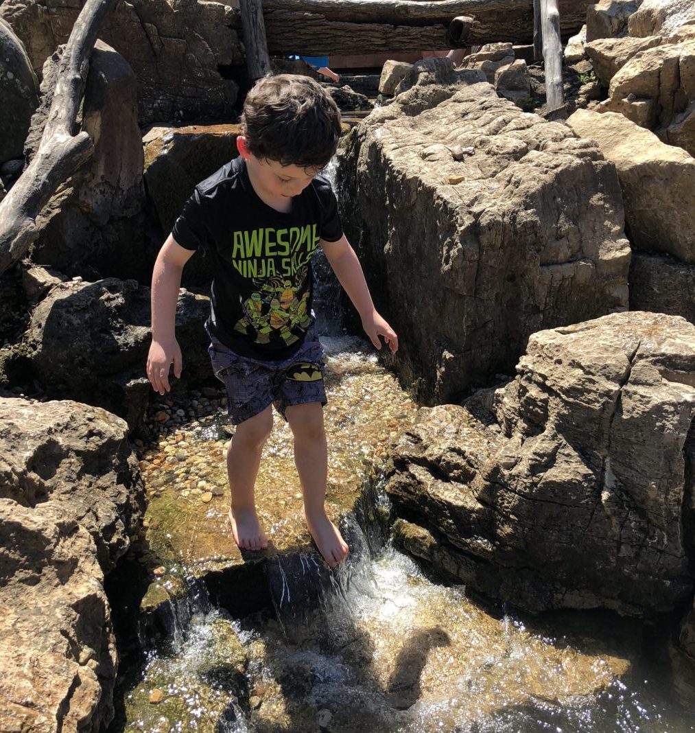 Boy talking in natural rocky creek bed swimsuit Peck Farm Geneva