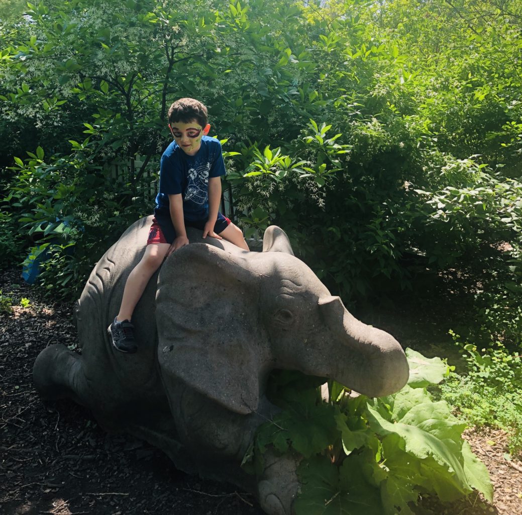 Kid riding elephant statue zoo gardens outside face painted Brookfield Zoo Hamill Family Play Zoo